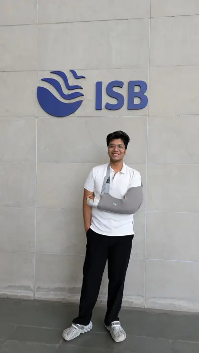 Eshan smiling in front of the ISB logo with his arm in a sling